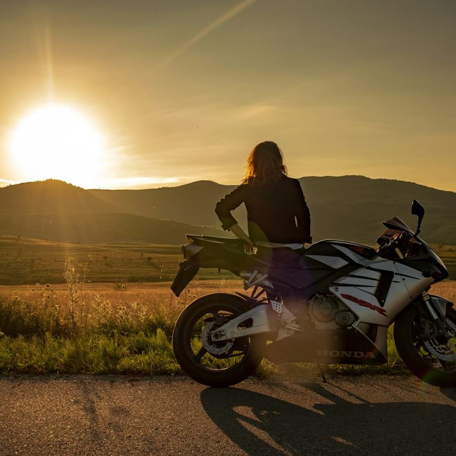 Mulher ao lado de uma moto esportiva ao pôr do sol