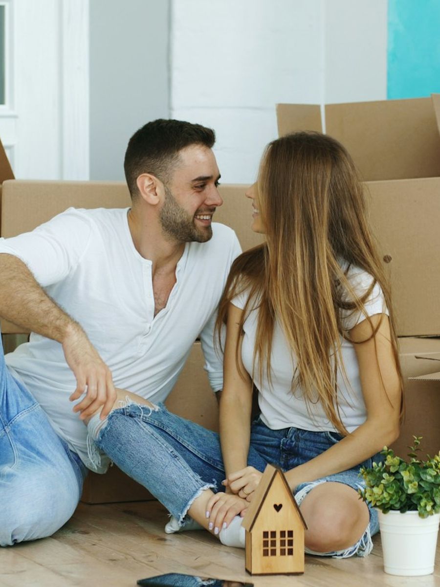 Casal sentado entre caixas de mudança segurando uma chave com chaveiro de casinha