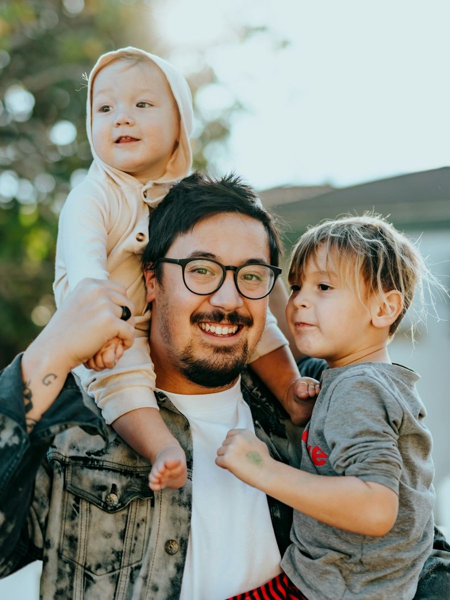 Pai sorrindo com os dois filhos no colo e nos ombros